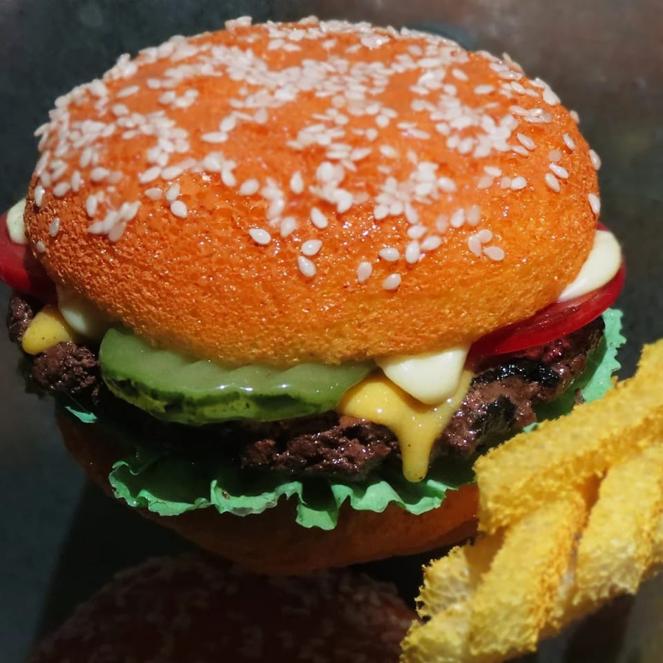 A Burger Palace burger with an orange bun, sesame seeds, lettuce, pickles, tomato, and cheese, with fries.
