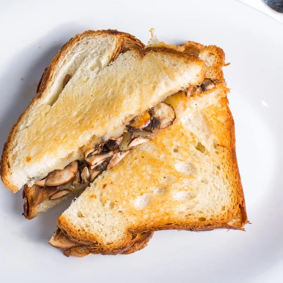 Toasted sandwich with melted cheese and sautéed mushrooms, cut in half on a white plate.