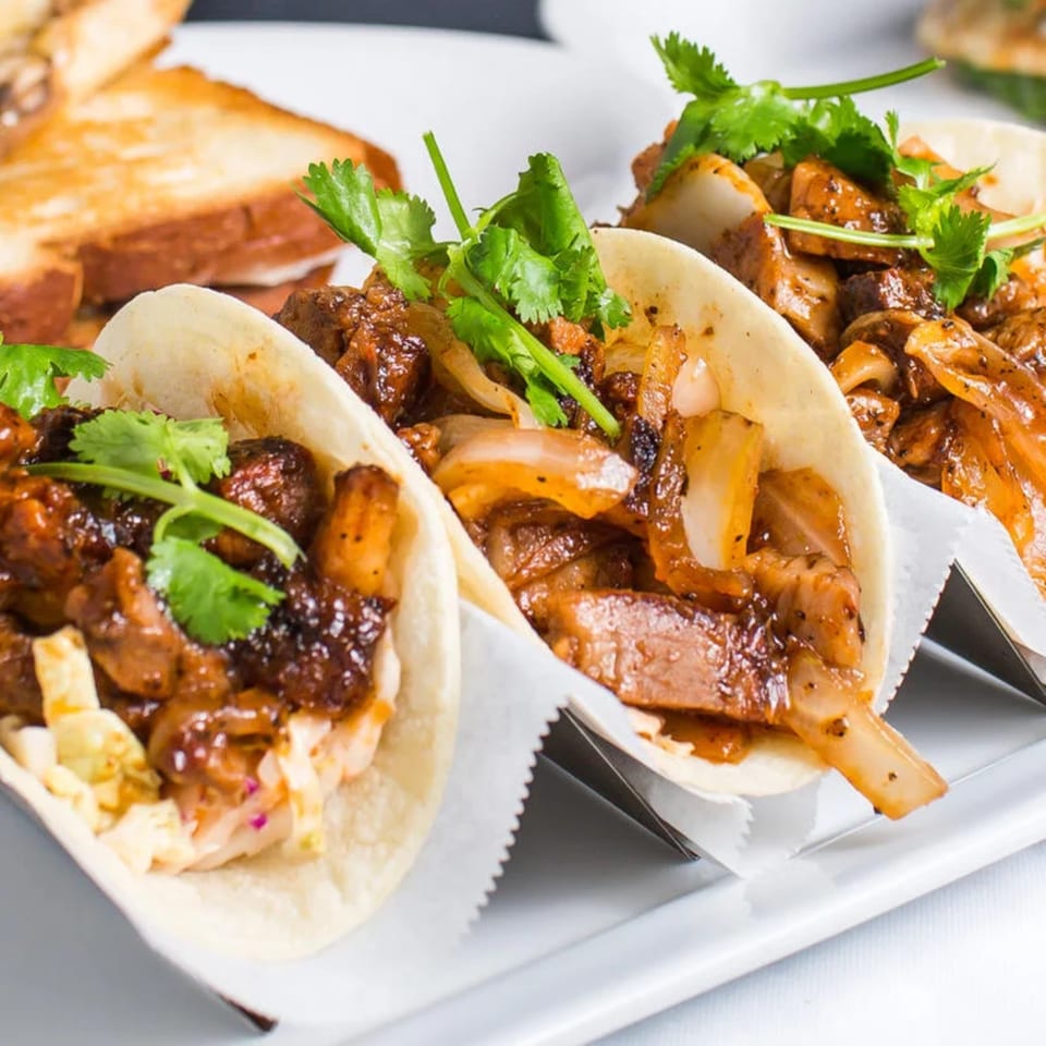 Three delicious tacos filled with meat, onions, and cilantro, served on a white plate.