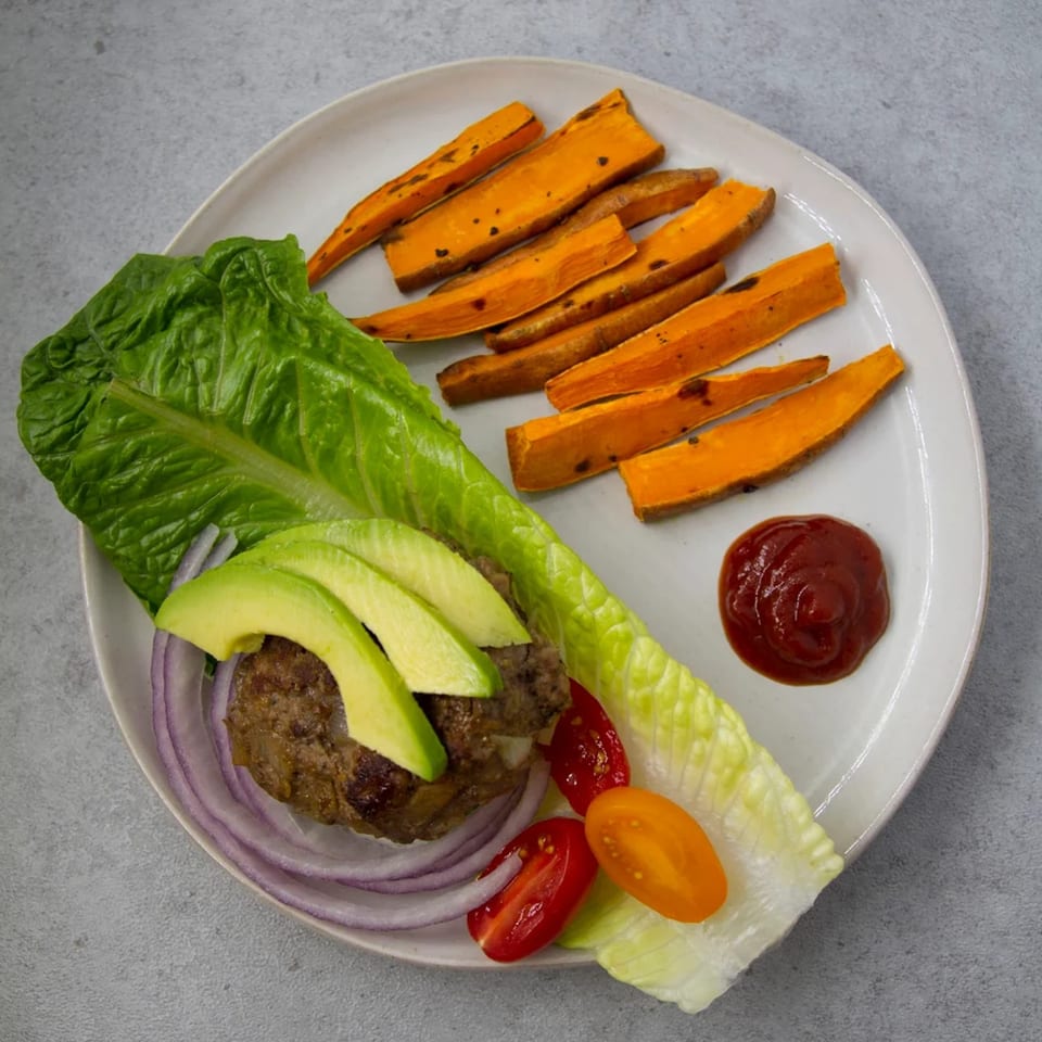 A lettuce-wrapped Burger Palace burger with avocado, onion, tomatoes, sweet potato fries, and ketchup.