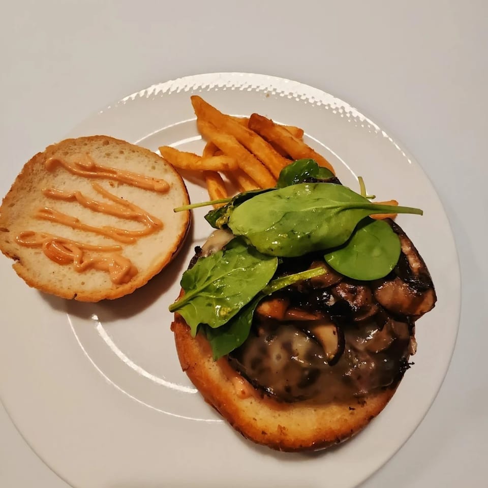 A mushroom and spinach burger with fries on a white plate at The Burger Palace.