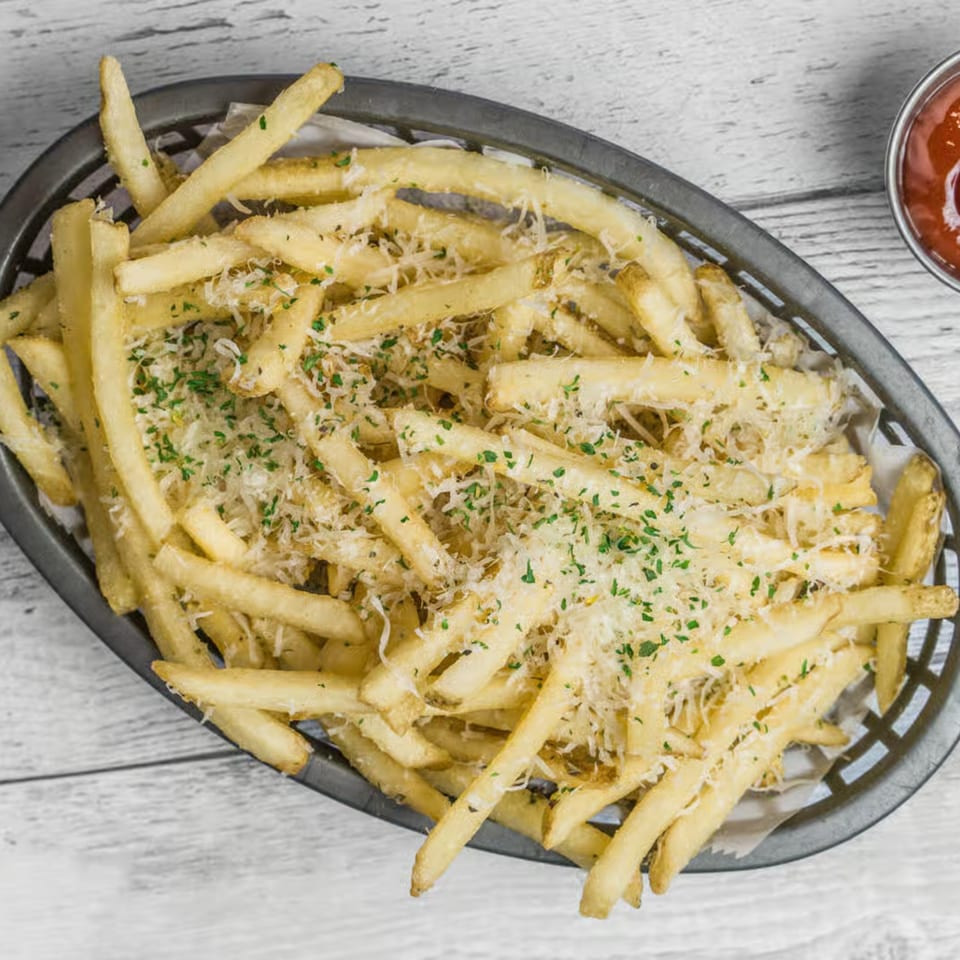 A basket of golden french fries topped with grated cheese and parsley, with a side of ketchup.