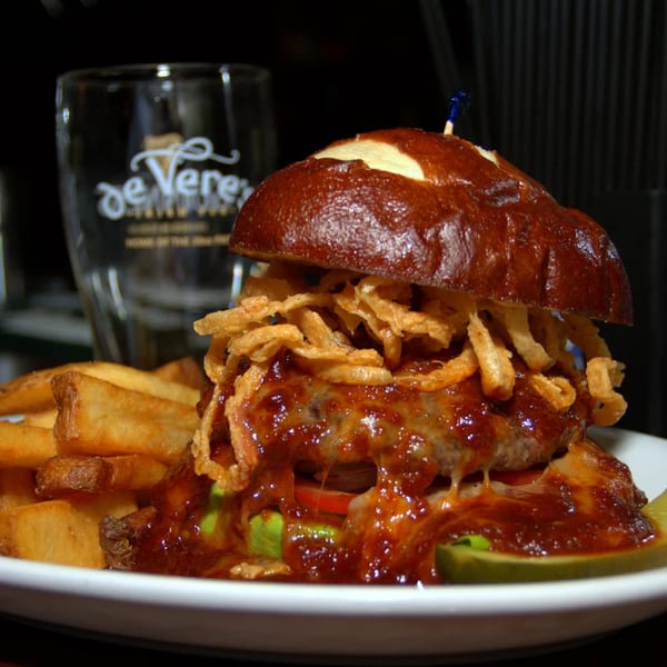 A Burger Palace burger with BBQ sauce, crispy onions, and fries on a white plate.