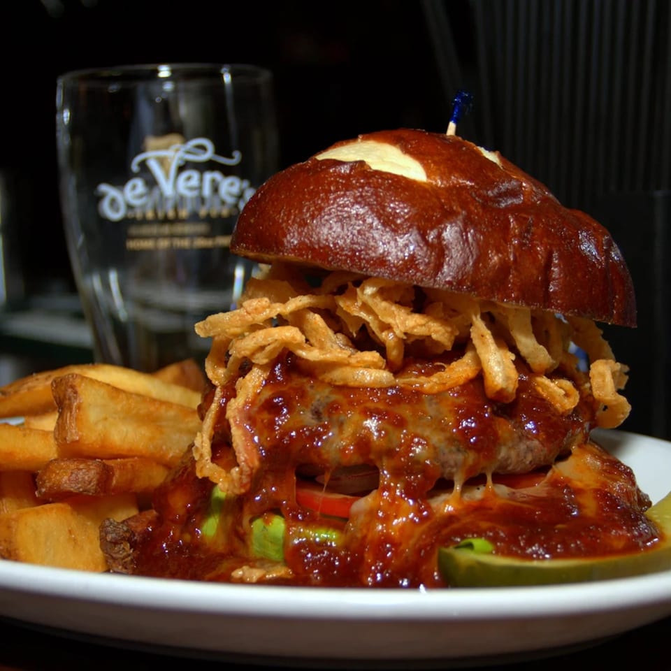 A Burger Palace burger with BBQ sauce, crispy onions, and fries on a white plate.