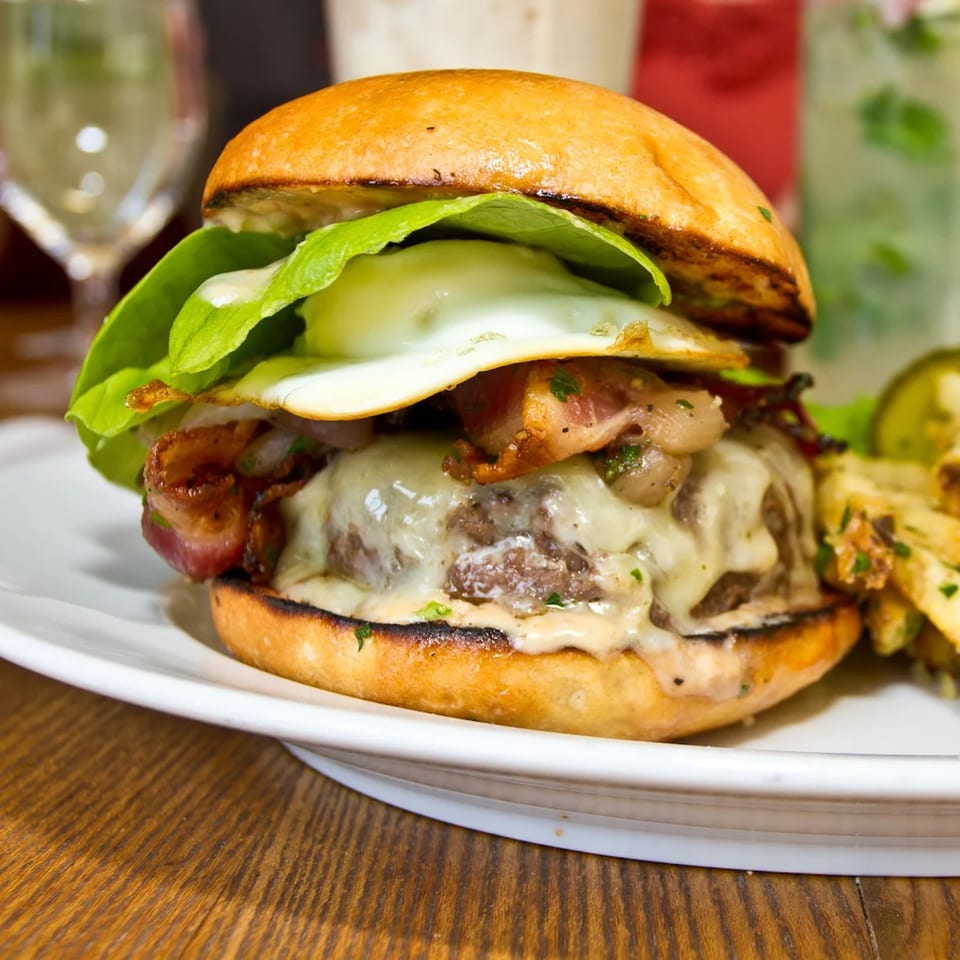 A Burger Palace burger with melted cheese, bacon, fried egg, lettuce, and sauce on a bun.