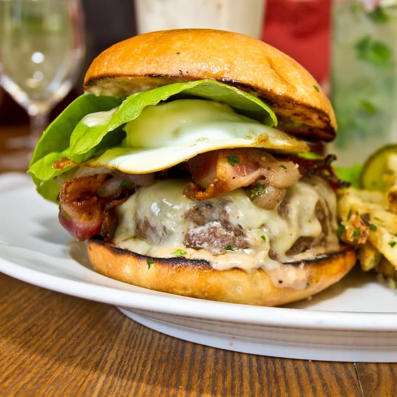 A Burger Palace burger with melted cheese, bacon, fried egg, lettuce, and sauce on a bun.