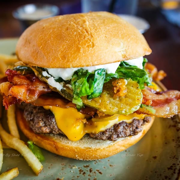 A juicy Burger Palace cheeseburger with bacon, lettuce, pickles, and sauce, served with fries.